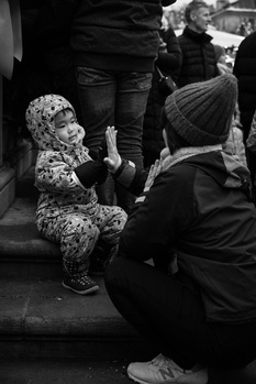 Adult crouching beside a young child on a street, engaged in conversation or interaction.