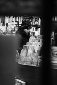 Person wearing winter hat and dark clothing browsing magazines or publications in an indoor retail space.