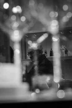 Black and white portrait of a person visible through a window with bokeh lights and reflections obscuring the view.