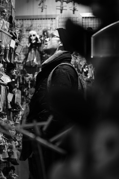 Person in dark hooded jacket viewed from behind in crowded urban alleyway with blurred storefronts.