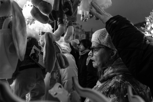 Man wearing glasses and a knit cap examines hanging meat cuts in a crowded market setting.