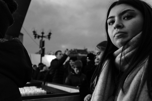 Woman in profile looking toward camera with contemplative expression, wearing scarf and earbuds in urban setting.