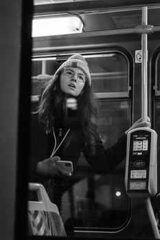 Woman with long hair standing in a bus doorway, looking upward in black and white.