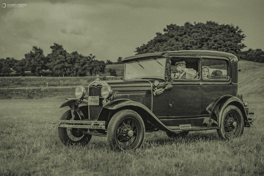Vintage automobile with passengers parked in an open field with trees in the background.