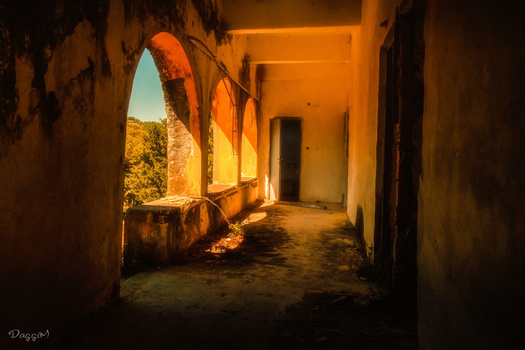 Sunlit arched stone corridor with warm golden light casting deep shadows on weathered walls.