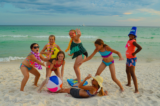 Group of children playing together on a beach with turquoise water and white sand.