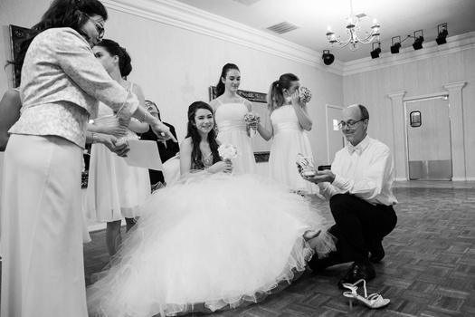 Bride in white tulle gown surrounded by wedding party members in an indoor venue with dramatic lighting.