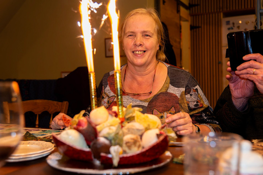 Woman at a table holding a smartphone while smiling at a birthday cake with lit candles.