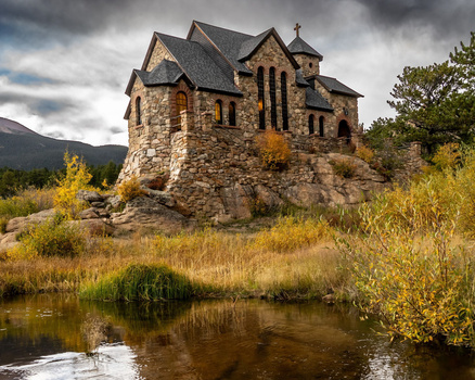 Stone castle with turrets beside a flowing stream surrounded by golden autumn vegetation.