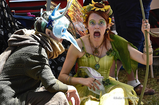 Person in green fairy costume with dramatic facial expression sitting next to costumed character with sword and armor.