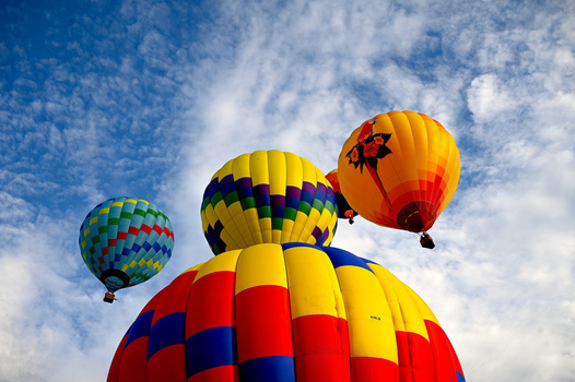 Four colorful hot air balloons against a blue sky with white clouds.