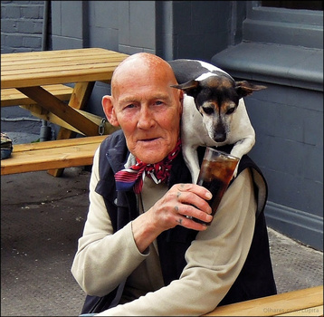 Man holding a tri-color dog while sitting at a wooden picnic table outdoors.
