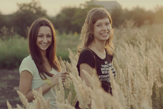 Two smiling young women posing together in a wheat field during golden hour.