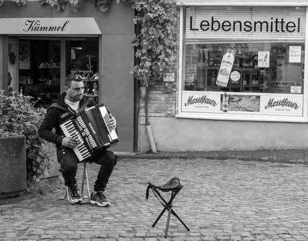 Street musician playing accordion outside storefronts in a European city square.