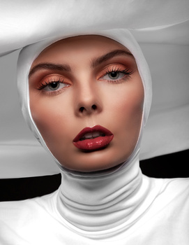 Woman with dramatic makeup and white fabric headwrap against minimalist background.