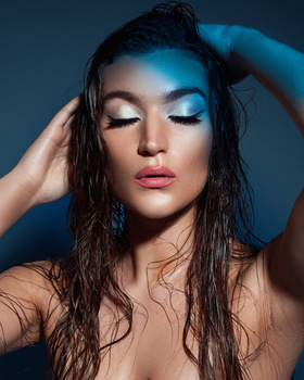 Woman with wet dark hair and blue eyeshadow against blue studio background.