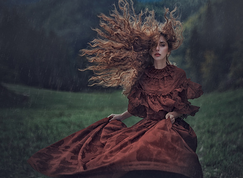 Woman in burgundy vintage dress with windswept hair in rainy outdoor setting.