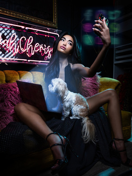 Woman holding white fluffy dog while taking selfie under neon signs in dark indoor setting.