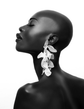 Profile portrait of a woman with shaved head wearing sculptural leaf-shaped earrings against white background.
