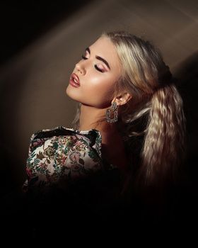 Woman in profile with long blonde hair wearing a sequined black garment against a dark background.