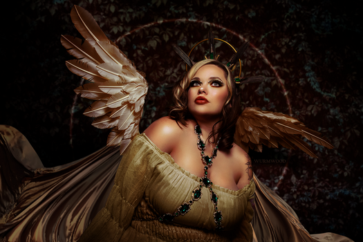 Woman with winged fairy costume and ornate gold headpiece against dark textured backdrop.