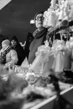 Woman in glasses and dark coat viewing frost-covered plants at close range in black and white.
