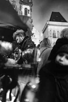 Cinematographer operating a camera on a crowded street at night with historic buildings and church spires in background.