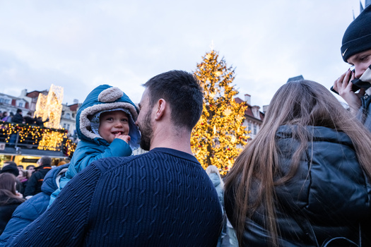 Man holding young child on shoulders at an outdoor holiday event with illuminated trees in background.