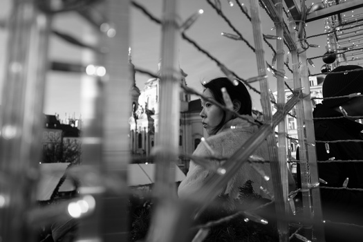 Woman in profile seated near illuminated storefront display windows at night.