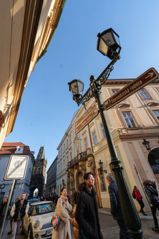 Street scene with historic architecture, ornate lamp post, and pedestrians under clear blue sky.