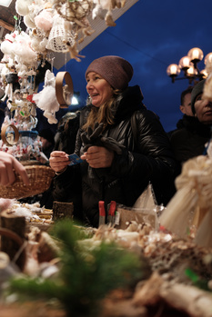 Woman in black leather jacket examining white floral arrangement at evening event.
