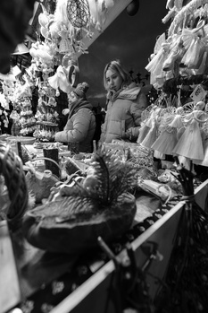Two people shopping at a decorated holiday market stall filled with ornaments and garland.
