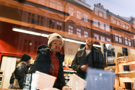 People viewed through storefront window with urban buildings reflected in glass at dusk.