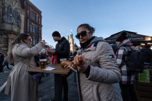 People enjoying food and drinks at an outdoor market or festival in a historic city square.