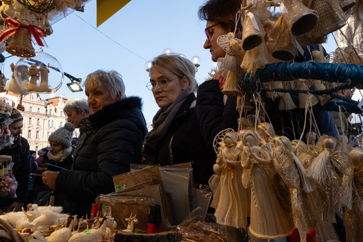 Shoppers browsing handmade wooden ornaments and decorations at an outdoor market stall.