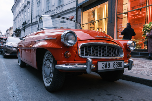 Red convertible vintage car parked on a European street lined with upscale storefronts.