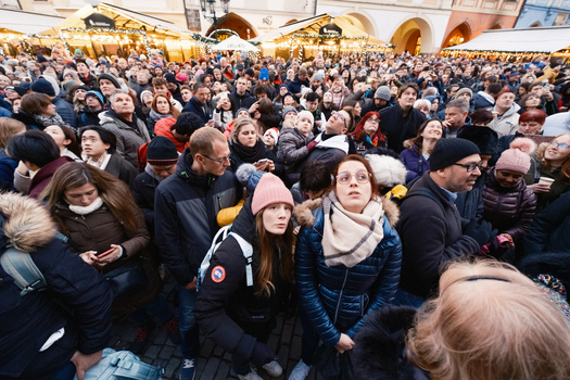 Dense crowd of people wearing winter clothing gathered in an indoor public space with arched ceiling.