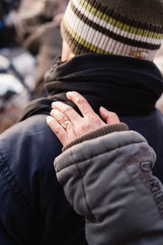 Close-up of clasped hands wearing winter gloves and a striped beanie in soft natural light.