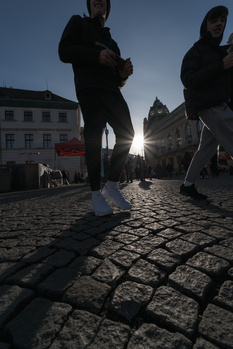 Runners jogging on a cobblestone street during golden hour with historic buildings silhouetted against a bright sky.