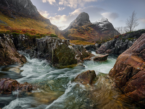 Turquoise river flowing through rocky Highland valley with steep mountains under partly cloudy sky.