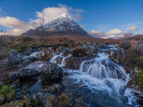Snow-capped mountain peak with cascading waterfall in foreground under blue sky.