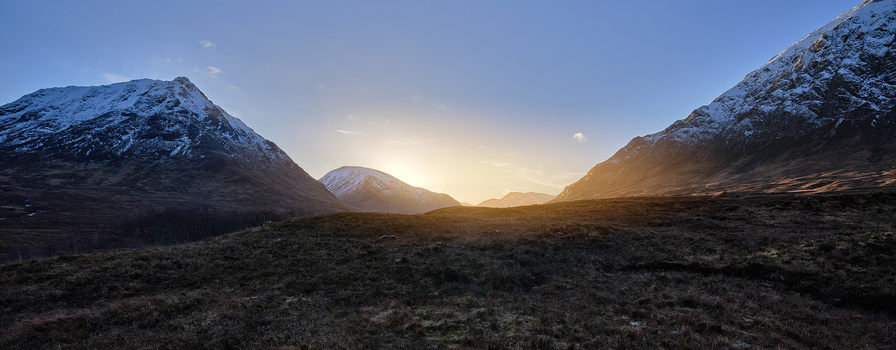 Snow-capped mountains flanking a valley at sunset, with warm golden light illuminating the landscape.