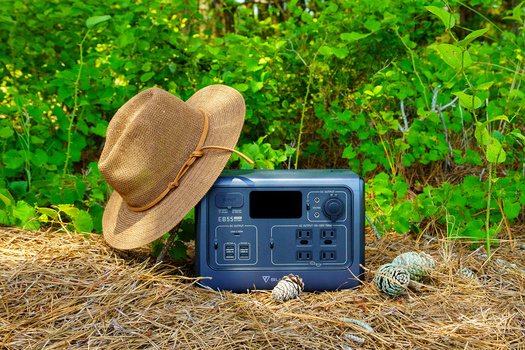 Portable power station with tan cowboy hat and coiled rope on straw ground against green foliage.