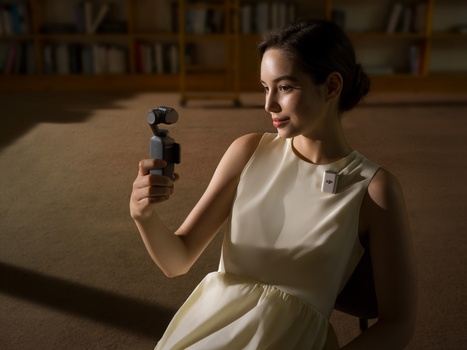Woman in light cream dress holding a compact gimbal stabilizer with three-axis stabilization.