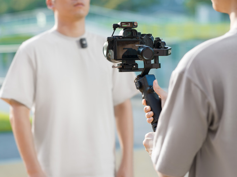 Videographer operating a gimbal-stabilized camera rig while filming two people outdoors.