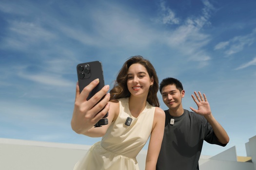 Two people taking a selfie outdoors against a bright blue sky with white clouds.