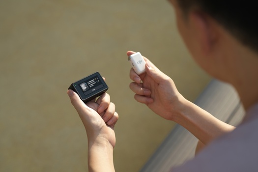 Person holding a black digital device in one hand and a white object in the other hand.
