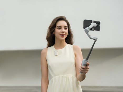 Woman in cream sleeveless dress holding a gimbal stabilizer with smartphone mounted on it.