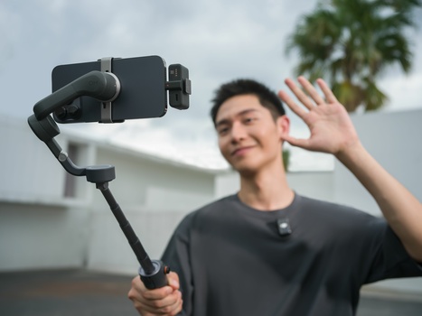 Content creator using a smartphone gimbal stabilizer while recording outdoors with palm trees in background.