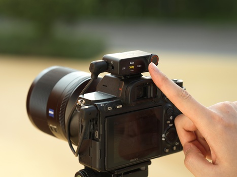 Photographer holding a mirrorless camera with attached external monitor and telephoto lens outdoors.